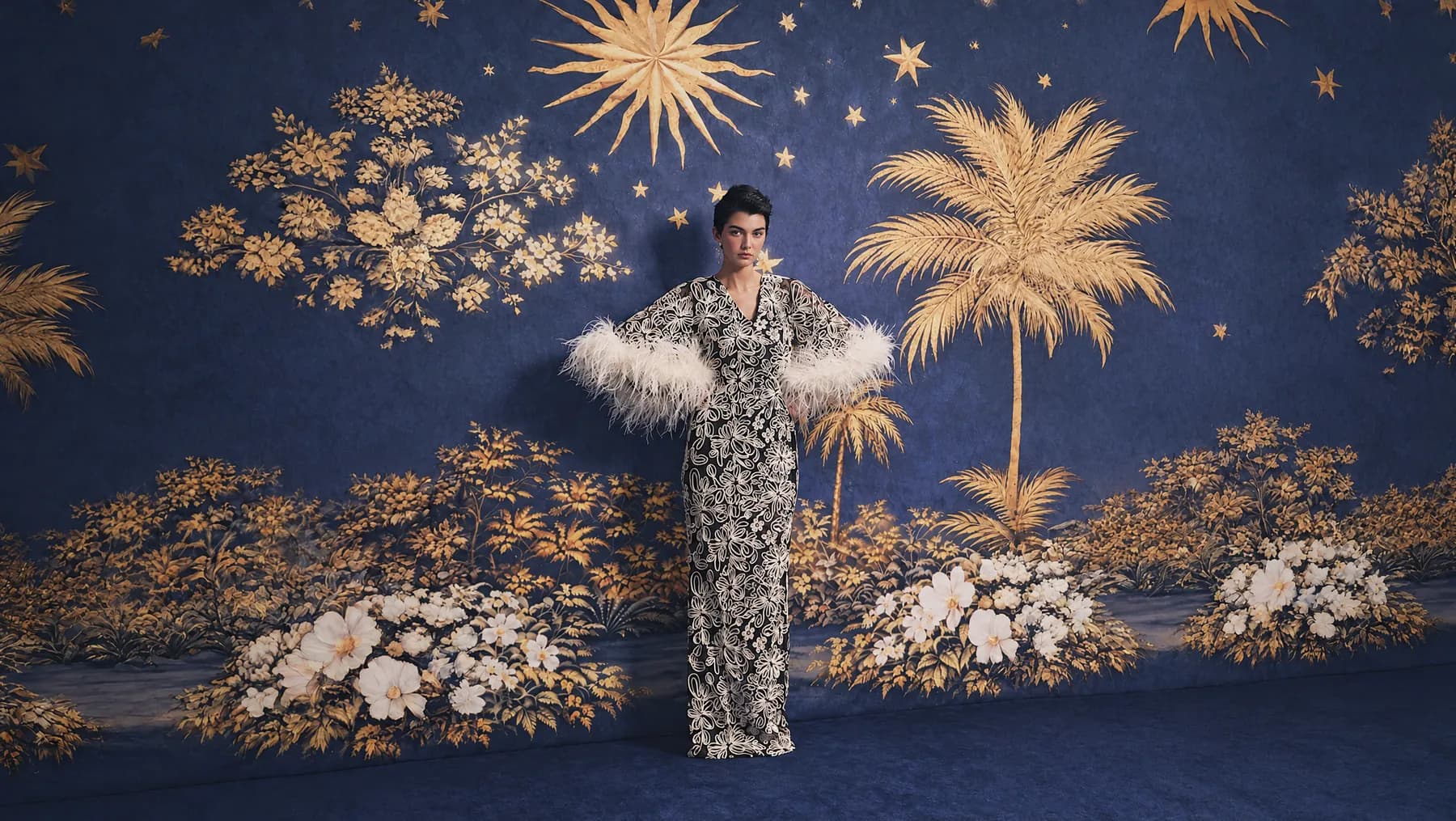 Model in a feathered gown against a midnight-blue painted backdrop