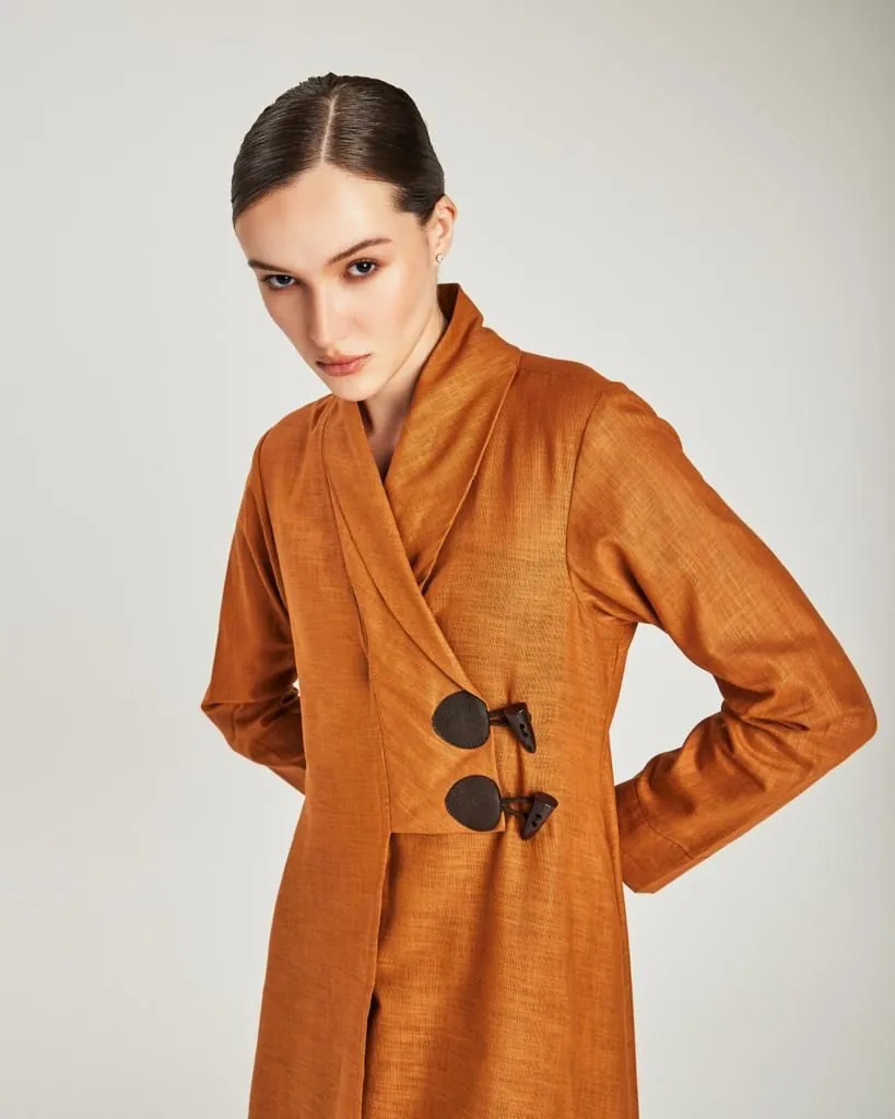 Model in a burnt-orange wrap coat studio portrait